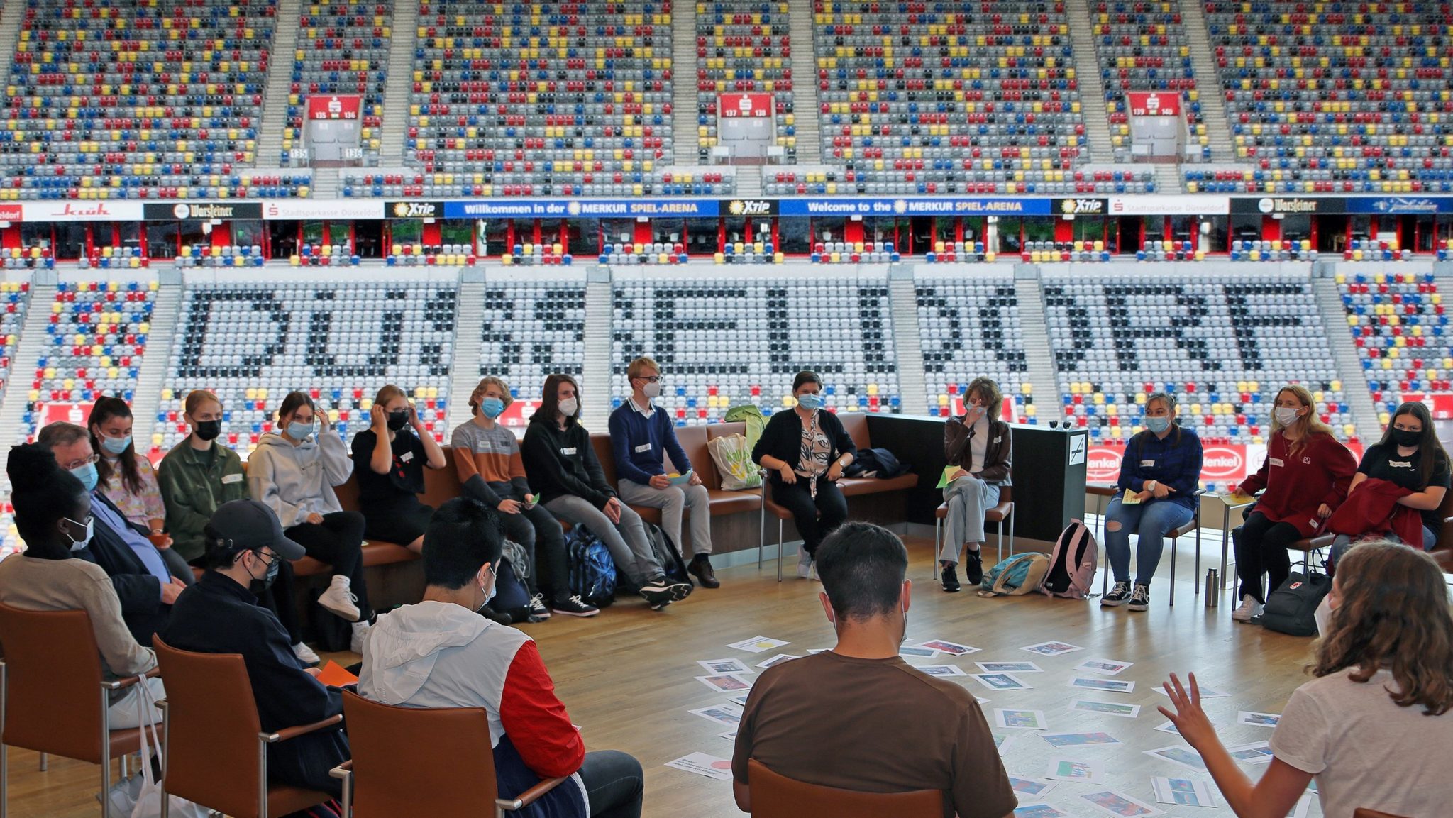Vordergrund: Schulklasse im Gespräch mit Politiker:innen; Hintergrund: Stadion Düsseldorf