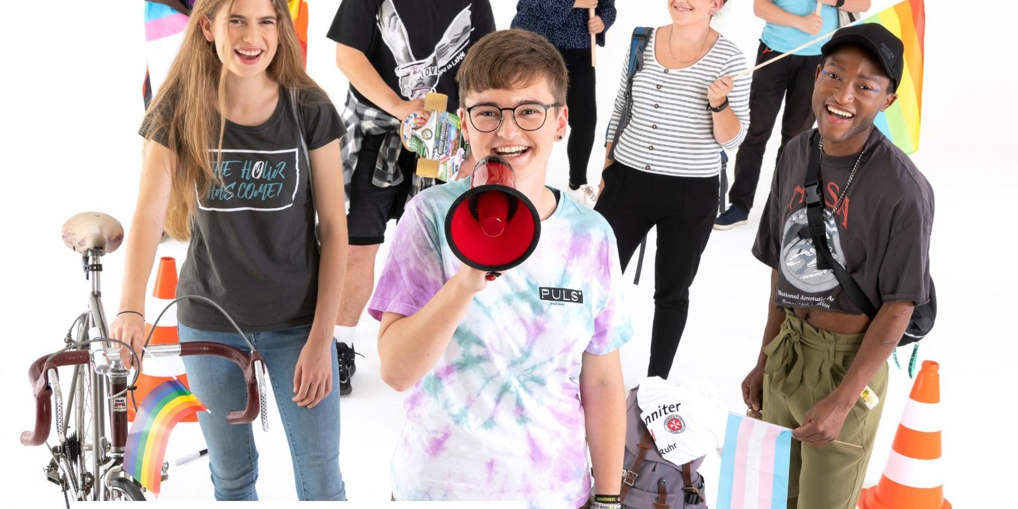 Vor weißem Hintergrund: Eine nachgestellte Straßendemonstration. Acht junge Menschen gucken lachend in die Kamera. Eine Teilnehmerin hält ein Megaphon, andere halten Regenbogenfahnen, ein Transparent "Kinder und Jugendrechte ins Grundgesetz" und eine Pappe mit "There is no planet B". Der Schriftzug über dem Motiv: "Wir sind deine Stimme!".