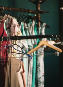 Im Vordergrund ist eine Kleiderstange mit vielen leeren Kleiderbügeln und einem Kleiderbügel mit Oberteil. Im Hintergrund ist eine voll behangene Kleiderstange zu sehen.