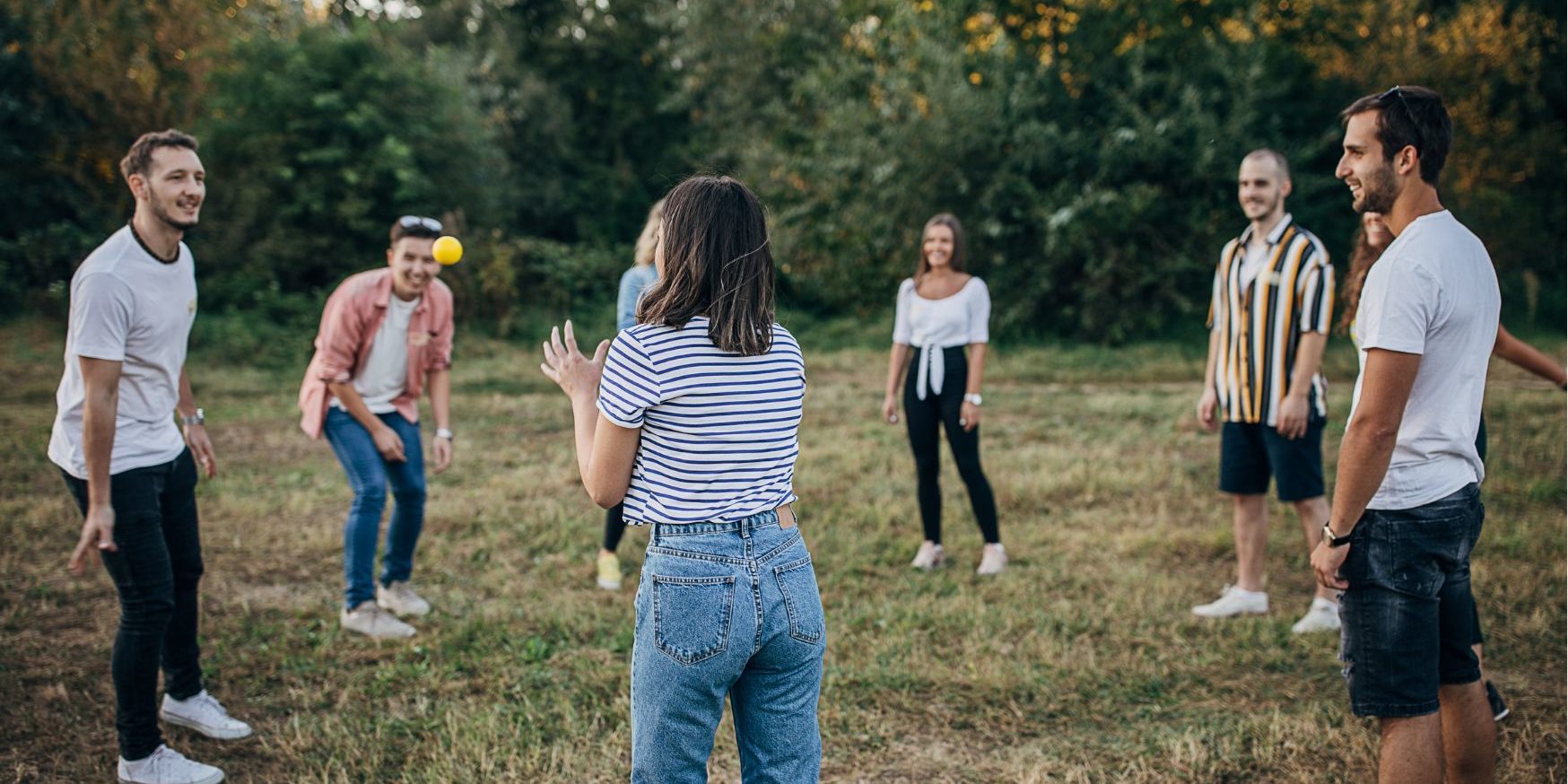 Juleica_Schulung Bild Auf einer Wiese stehen sieben junge Erwachsene in einem Kreis und spielen ein Gruppenspiel mit einem kleinen Ball