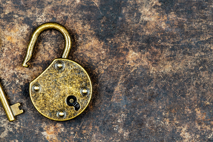 Am rechten Bildrand liegen, vor einem dunklen HIntergrund ein goldener Schlüsel und ein Schloss. Beide sehen alt aus.