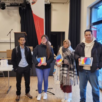 20231220_131612 Junge Menschen stehen nebeneinander und schauen in die Kamera. 3 halten ein Ipad in der Hand,